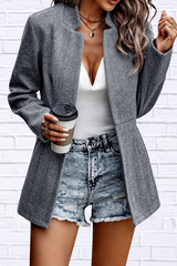 Person wearing a gray blazer, white top, and denim shorts holding a coffee cup against a white brick wall.